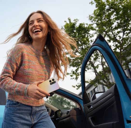 Eine lachende Person mit Handy in der Hand steigt aus einem blauen Auto