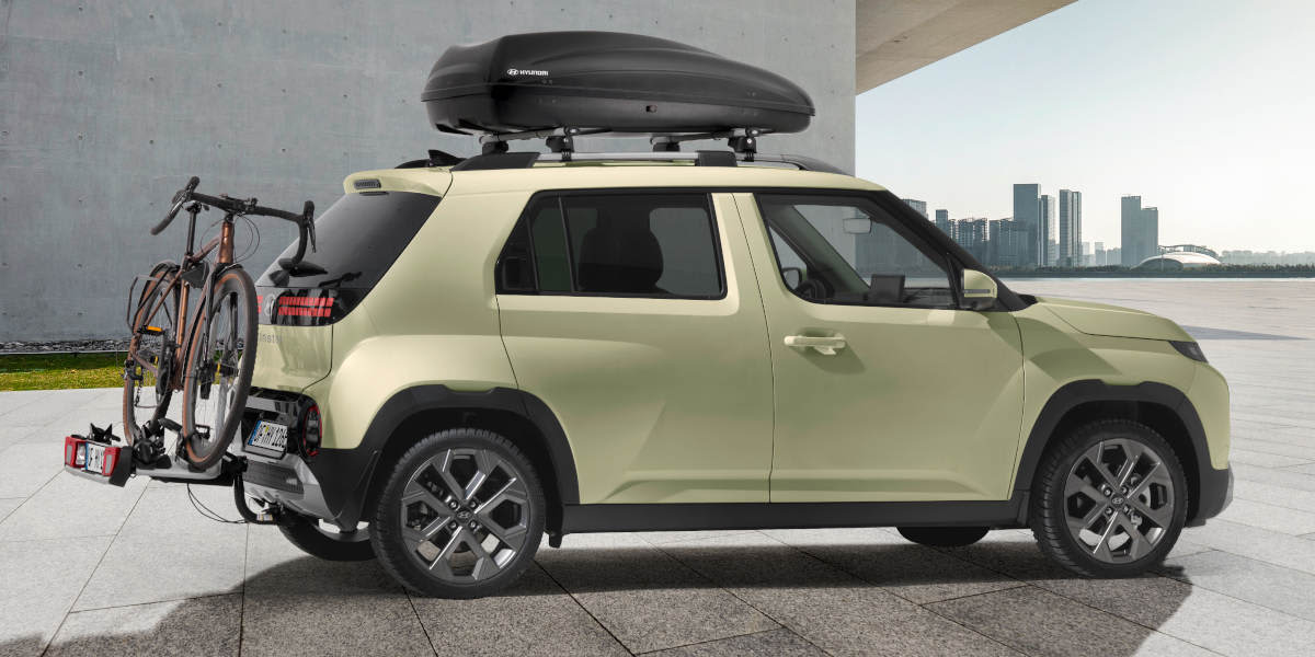 Hyundai Inster mit Zubehör: Dachträger, Fahrradträger. Seitliche Ansicht.