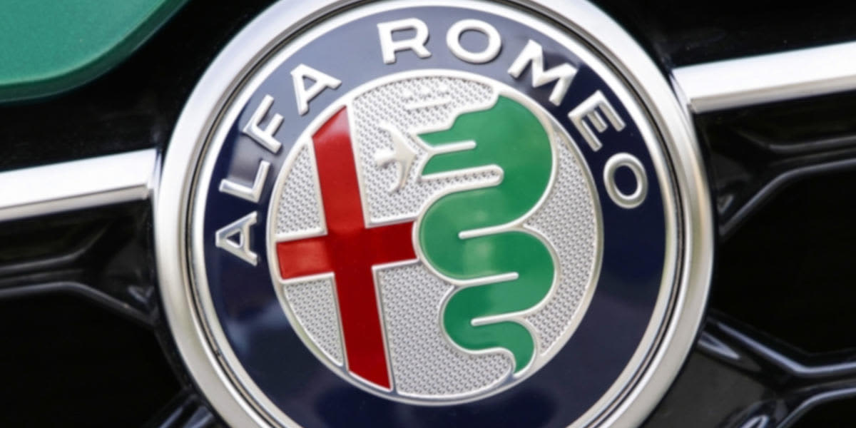 Eine Nahaufnahme des farbigen Alfa-Romeo-Logos, das schräg auf dem dunkelgrauen Kühlergrill eines Fahrzeugs angebracht ist.