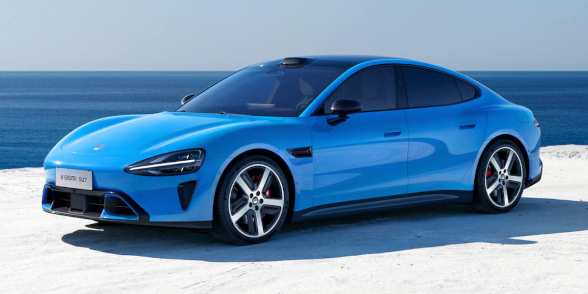 Eine leuchtend blaue Xiaomi SU7 Elektro-Limousine steht auf hellem Untergrund vor einer tiefblauen Meereskulisse.