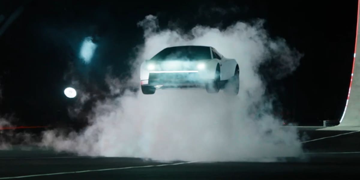 Ein weißer Sportwagen schwebt über einer dichten Rauchwolke bei Nacht. Die leuchtenden Frontscheinwerfer und die flache Silhouette wirken spektakulär.