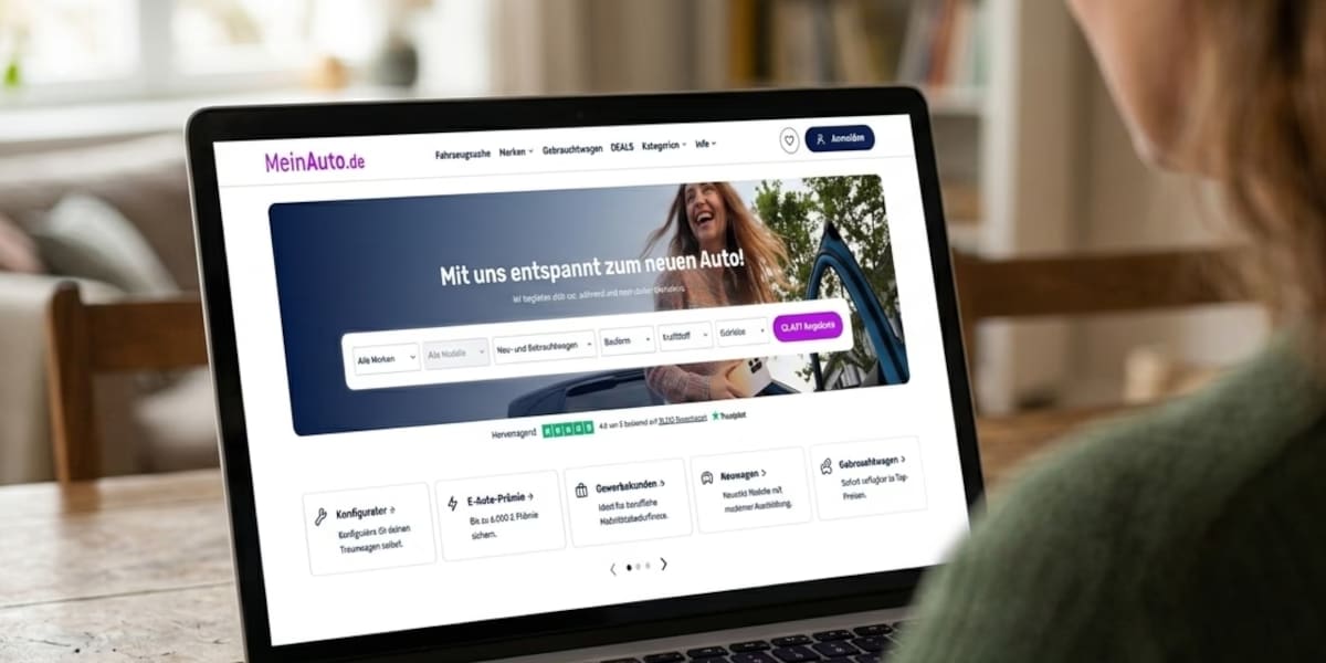 KI-generiertes Bild: Ein geöffneter Laptop auf einem Holztisch zeigt die Website MeinAuto.de mit Suchmaske, während im Vordergrund eine Person von hinten zu sehen ist.