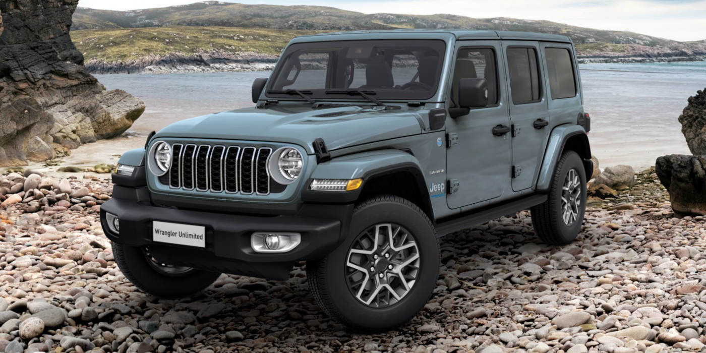 Ein graublauer Jeep Wrangler Unlimited steht an einem steinigen Küstenabschnitt. Prägend sind der klassische Sieben-Schlitz-Grill und das markante Offroad-Design.   