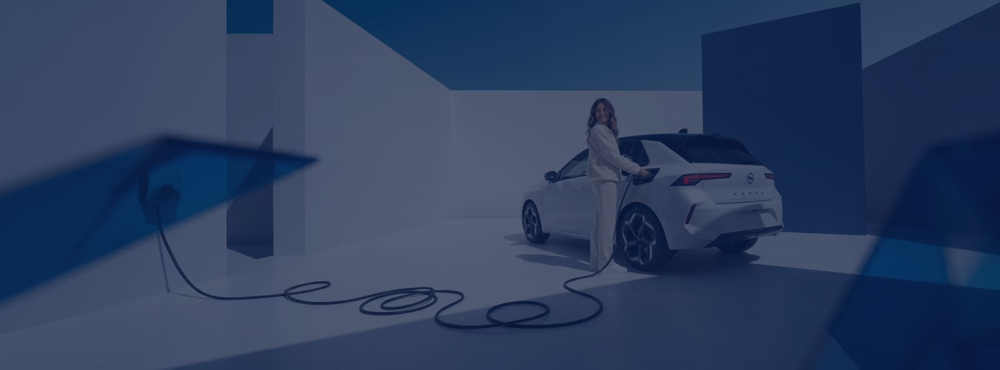 Eine lächelnde Frau lädt einen weißen Opel Corsa Electric an einem Ladekabel auf. Die Szene ist in einer minimalistischen, modernen Studiokulisse mit weißen Wänden und blauem Himmel inszeniert, überlagert von einem kühlen, dunkelblauen Farbfilter.