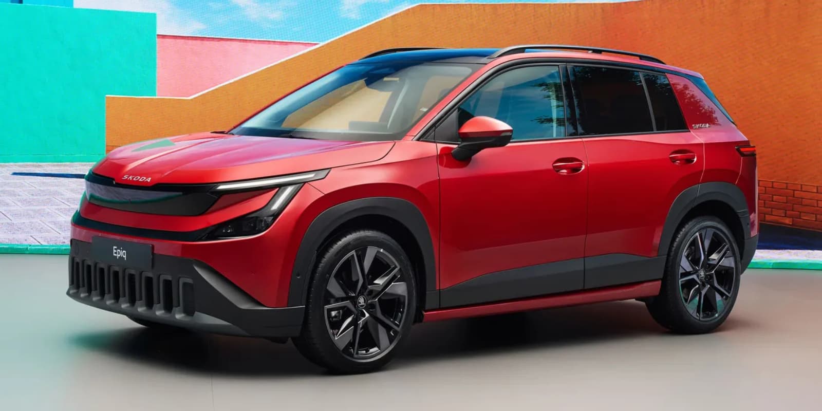Ein roter Skoda Epiq Elektro-SUV steht vor buntem Hintergrund. Prägend sind die schmalen Scheinwerfer und dunkle Verkleidungen.