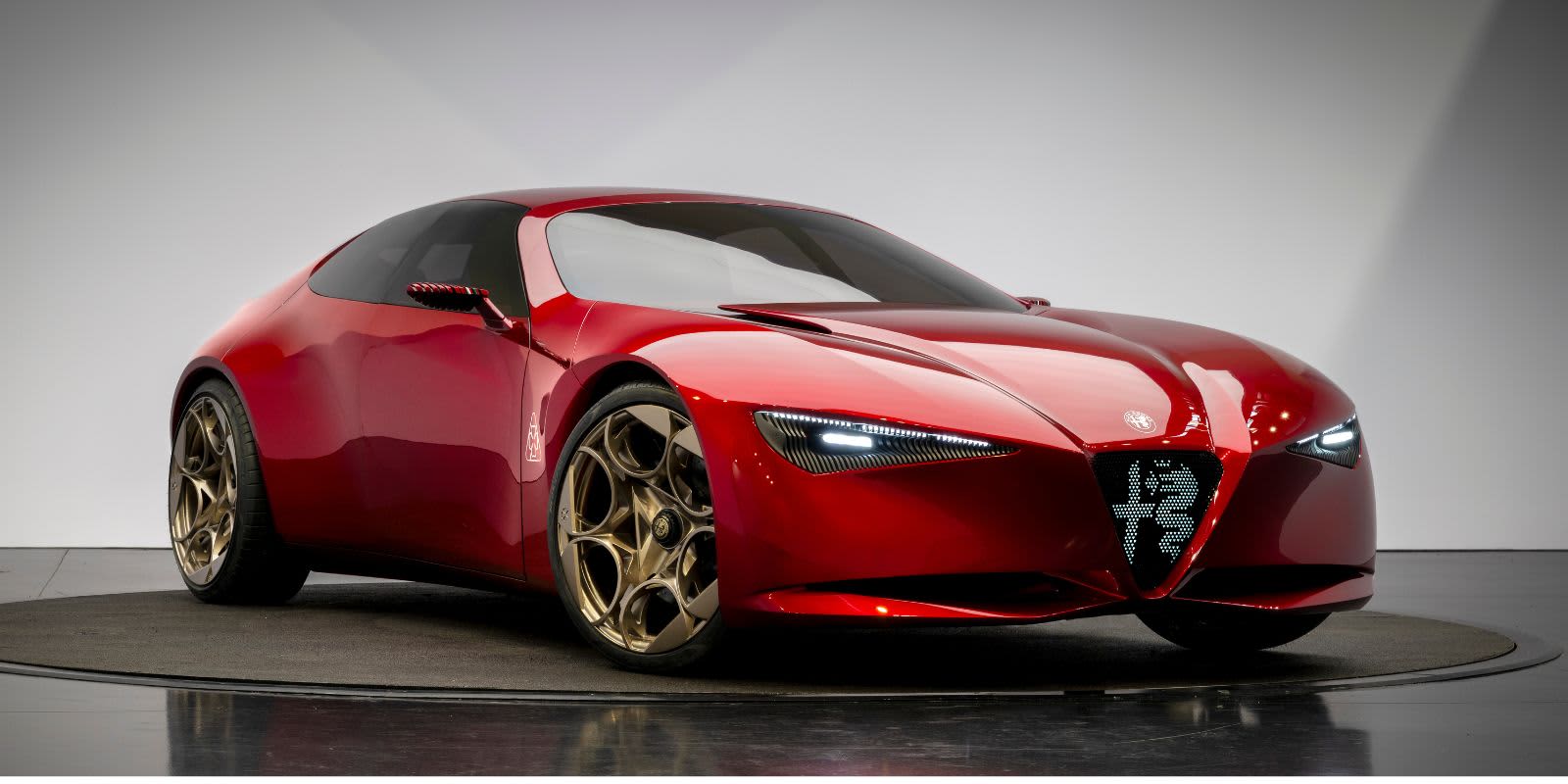 Ein roter Alfa Romeo Concept steht im Studio. Er besticht durch seine fließende Coupe-Form, das leuchtende Scudetto-Herzelement und goldene Felgen.