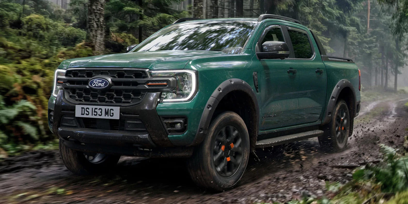 Ein dunkelmünzgrüner Ford Ranger Pickup fährt auf einem matschigen Waldweg. Auffällig sind die markanten C-förmigen LED-Scheinwerfer und Offroad-Details.