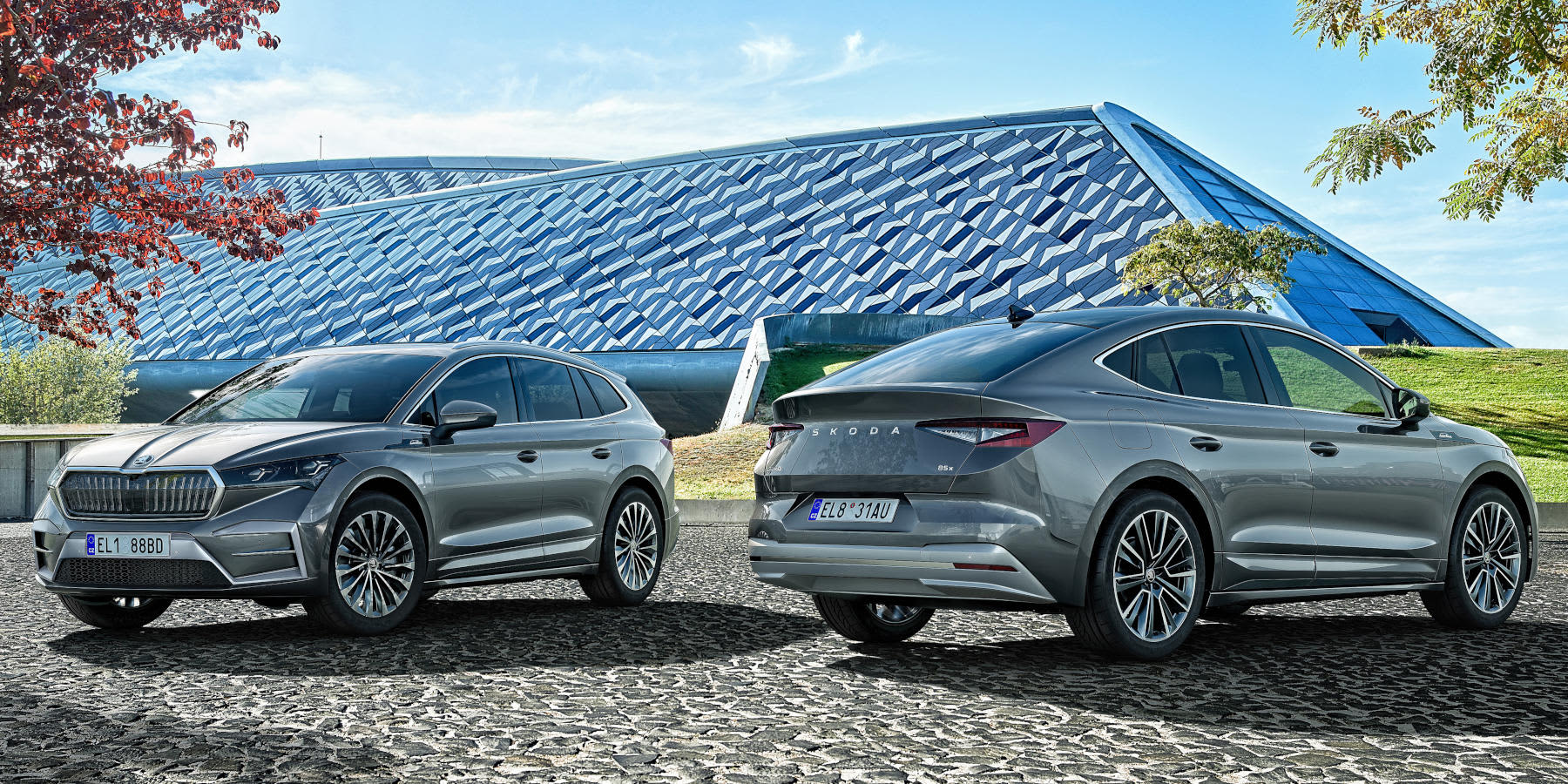  Skoda  Enyaq und Enyaq Coupe in der Sonne unter Bäumen auf einem Parkplatz