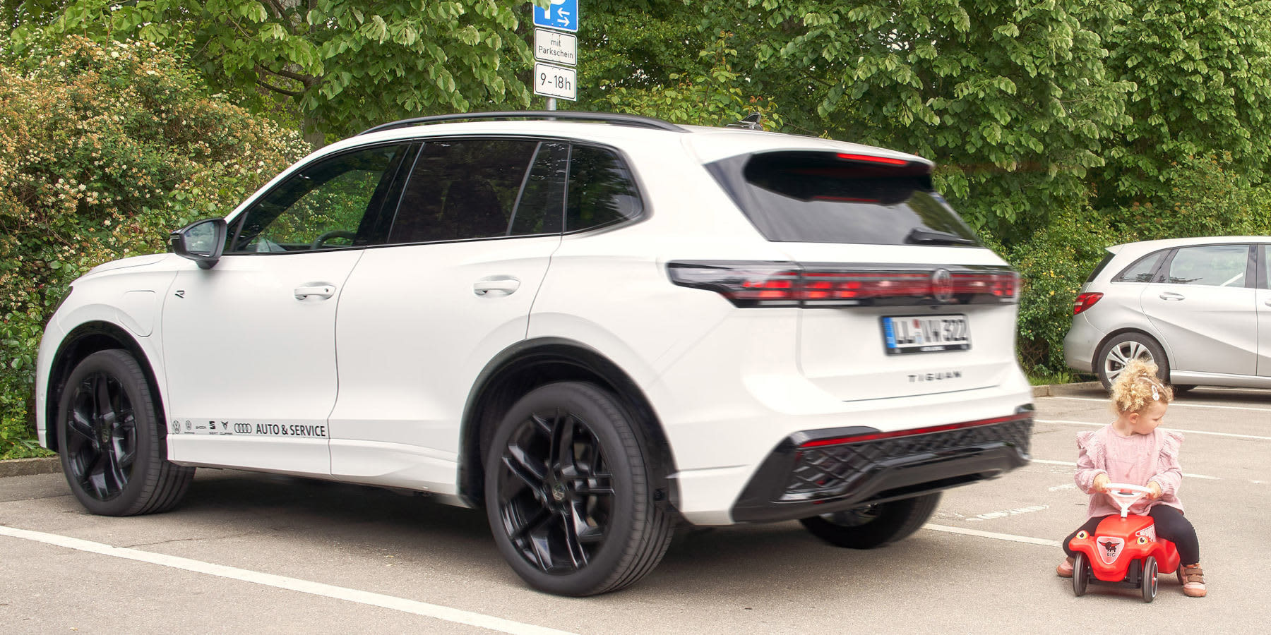 Kleinkind auf Bobbycar hinter einem weißen SUV