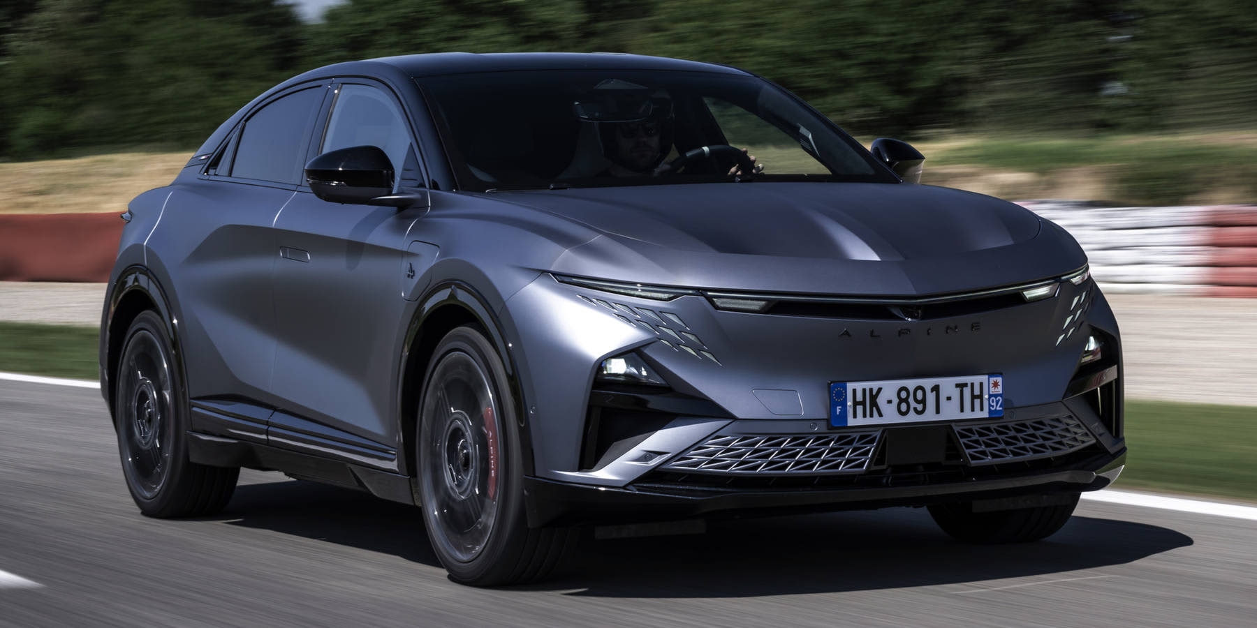 Ein mattgrauer Alpine A390 GTS fährt dynamisch auf einer Rennstrecke. Das Crossover hat ein französisches Kennzeichen (HK-891-TH) und schmale LEDs.
