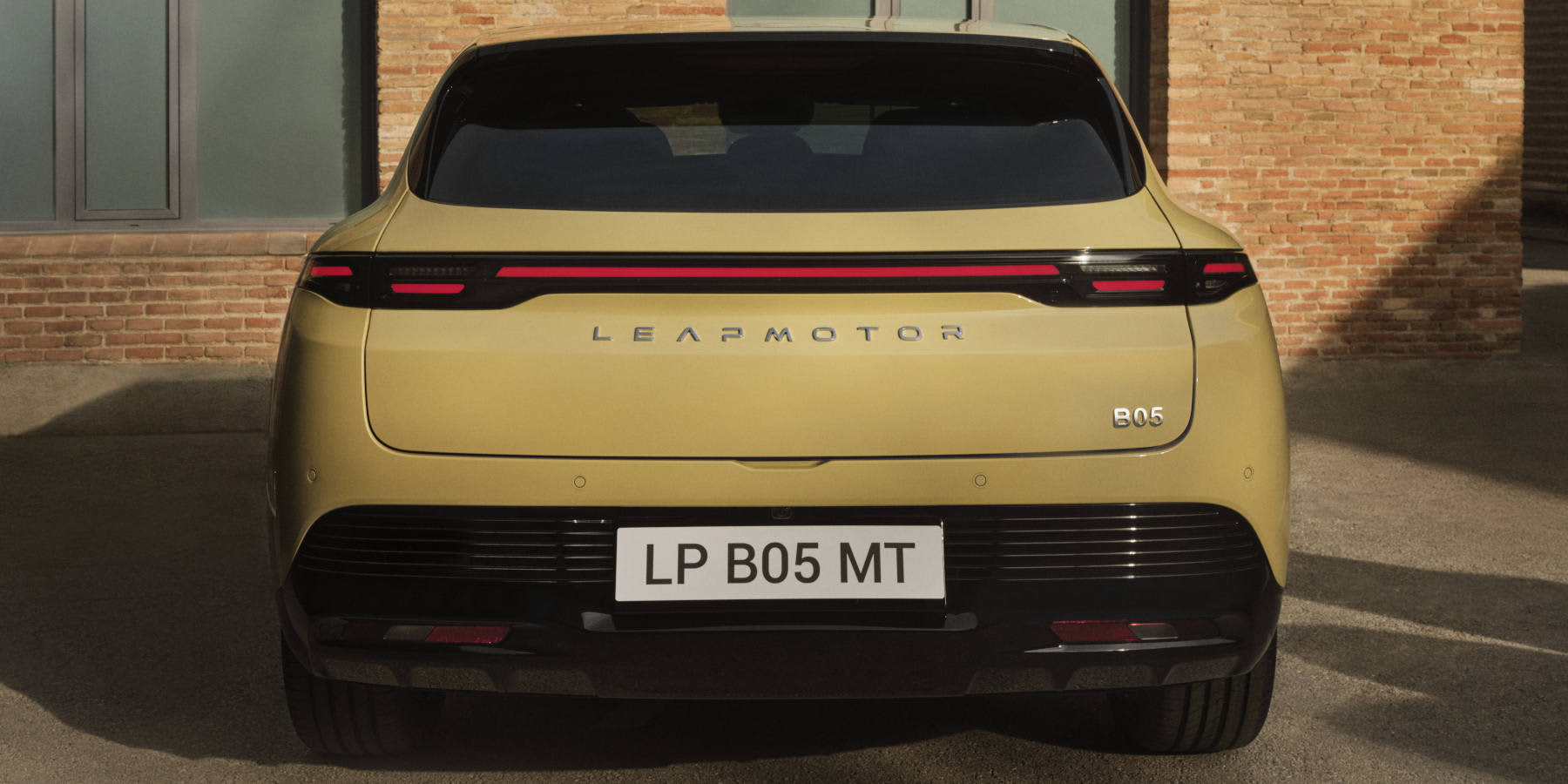 Die Heckansicht eines gelben Leapmotor B05. Zu sehen sind ein durchgehendes Leuchtenband, der zentrale Markenschriftzug sowie das Kennzeichen „LP B05 MT“ vor einer Backsteinwand.