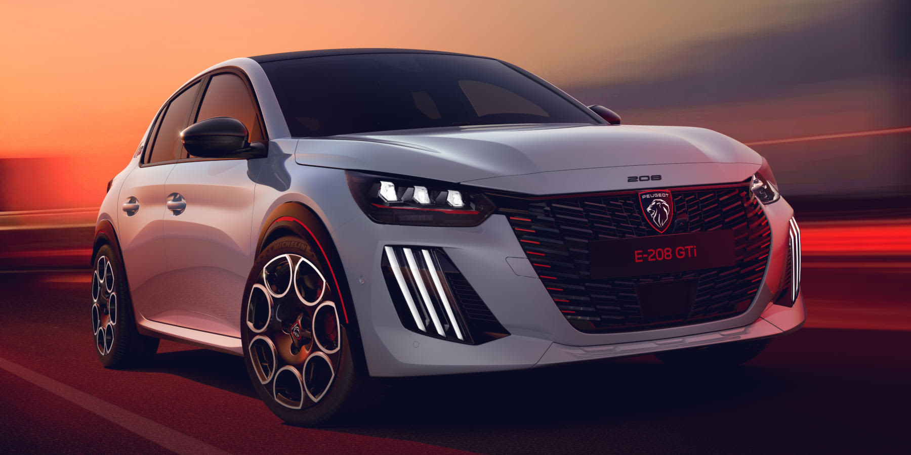 Ein weißer Peugeot E-208 GTi fährt bei Sonnenuntergang. Das sportliche Kompaktauto aus der Datei PEUGEOTE-208GTi.jpg zeigt markante dreiteilige LED-Tagfahrlichter und auffällige Felgen.