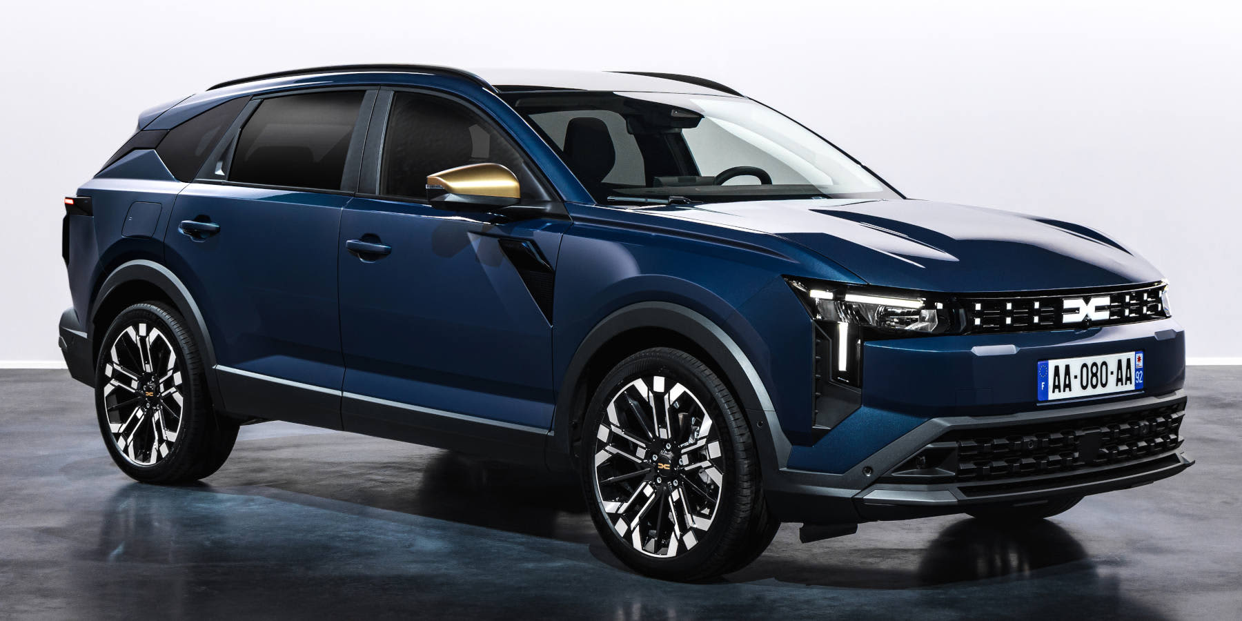 Schrägansicht eines dunkelblauen Dacia-SUVs mit weißem Dach, goldfarbenen Spiegelkappen, markanten Alufelgen und französischem Kennzeichen in einer Studio-Umgebung vor Weiß. (KI-generiert)