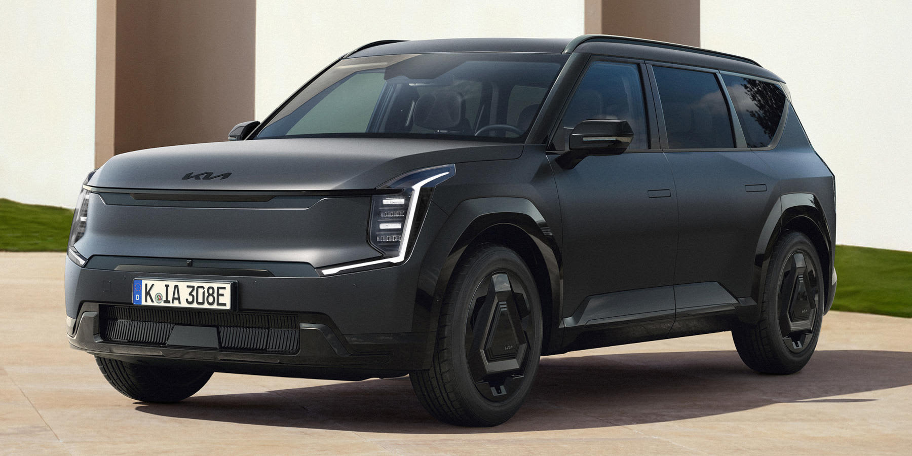 Ein robuster, mattschwarzer Kia EV9 steht vor hellen architektonischen Säulen im Freien. Das Elektro-SUV prägen vertikale LED-Scheinwerfer, markante aerodynamische Felgen und eine kantige Formgebung.