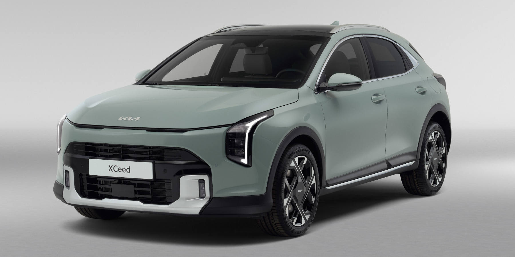 Schrägansicht eines hellgrün-grauen Kia XCeed Crossovers vor einem neutralen, hellgrauen Hintergrund. Das Fahrzeug verfügt über ein schwarzes Panorama- oder Kontrastdach.