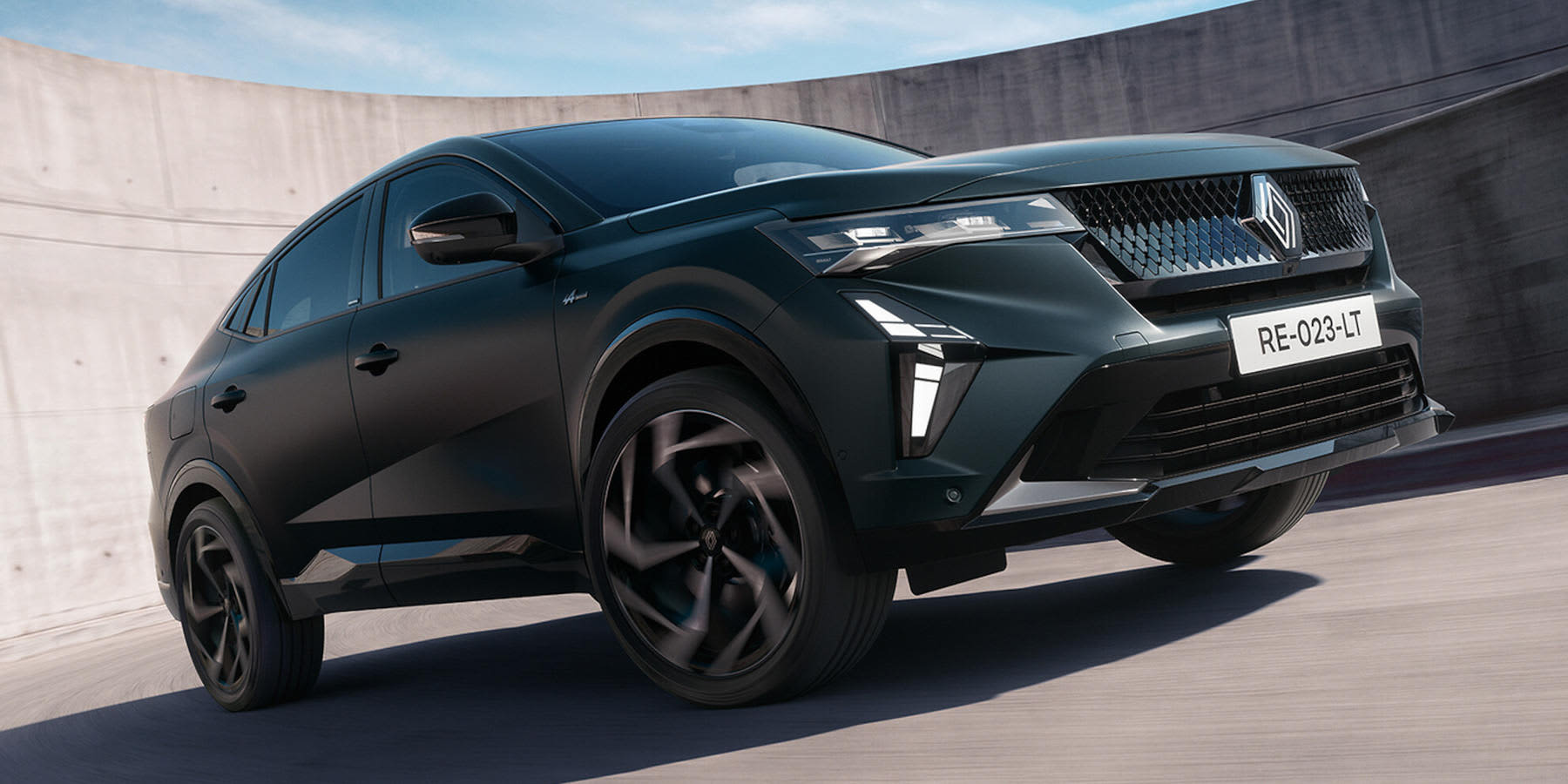 Ein dunkler Renault Rafale fährt an einer Betonwand entlang. Markant sind das Coupé-SUV-Design, der Rautengrill und die LED-Lichtsignatur.   