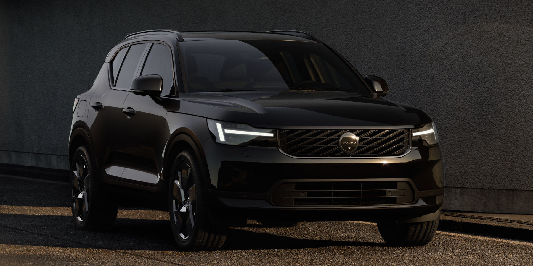 Ein schwarzer Volvo XC40 SUV steht schräg vor einer dunklen Wand. Prägend sind das LED-Lichtdesign ("Thors Hammer") und der Frontgrill.