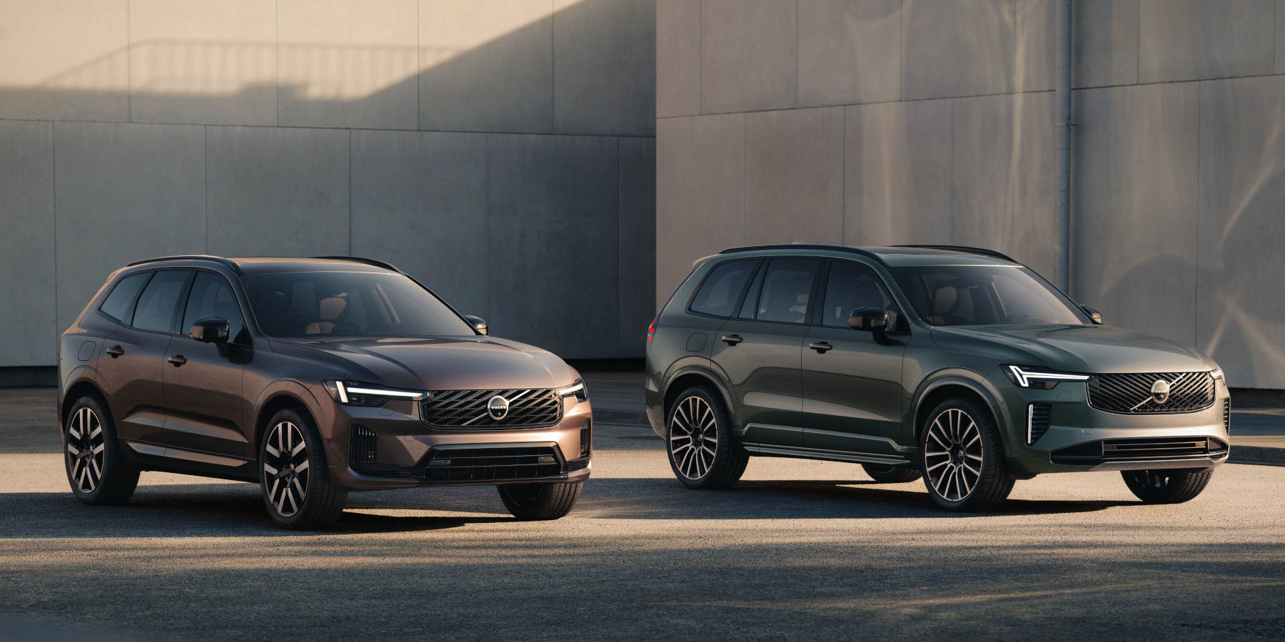 Zwei Volvo SUVs, ein XC60 und ein XC90, stehen nebeneinander vor einer Betonwand. Markant sind die "Thors Hammer"-LED-Scheinwerfer.  