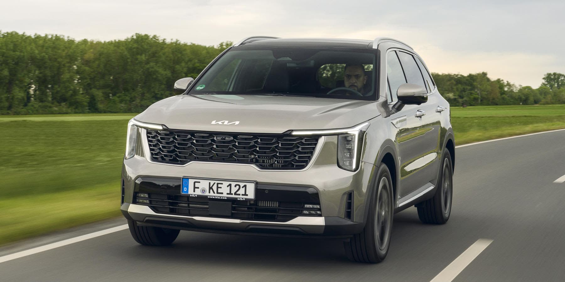 Ein silberner Kia Sorento fährt auf einer Landstraße. Das moderne SUV zeigt sich mit markantem Frontgrill, vertikalen LED-Scheinwerfern und klaren Linien.   