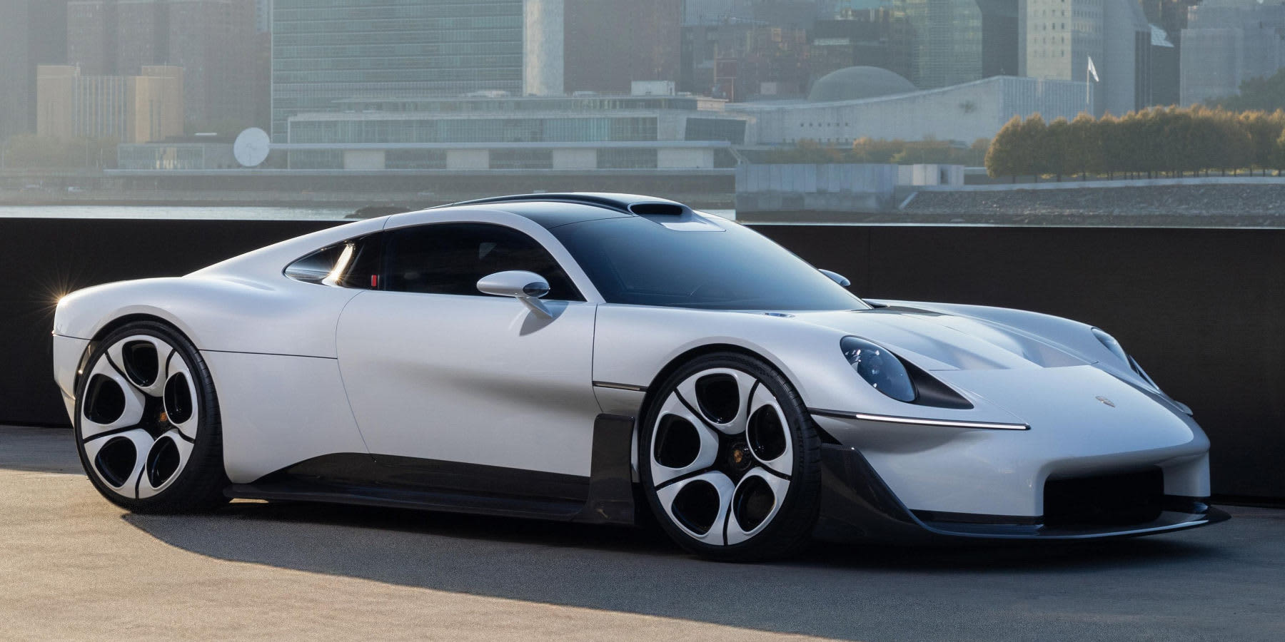 Ein silberner Porsche Mission S steht vor einer Skyline-Kulisse. Auffällig sind die tiefe Hypercar-Silhouette, ovale LED-Scheinwerfer und große Fünf-Speichen-Felgen.