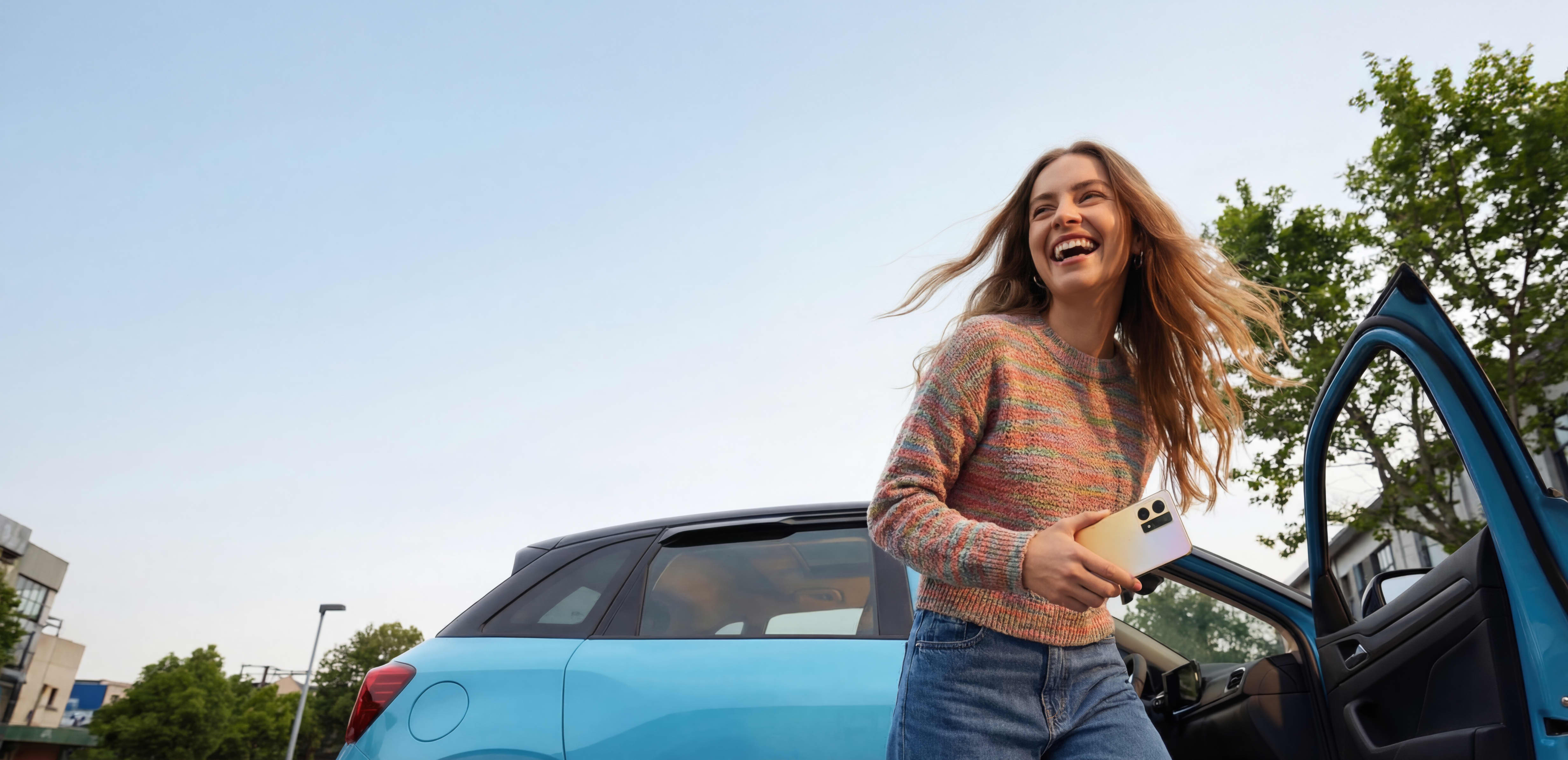 Eine lachende Person mit Handy in der Hand steigt aus einem blauen Auto aus
