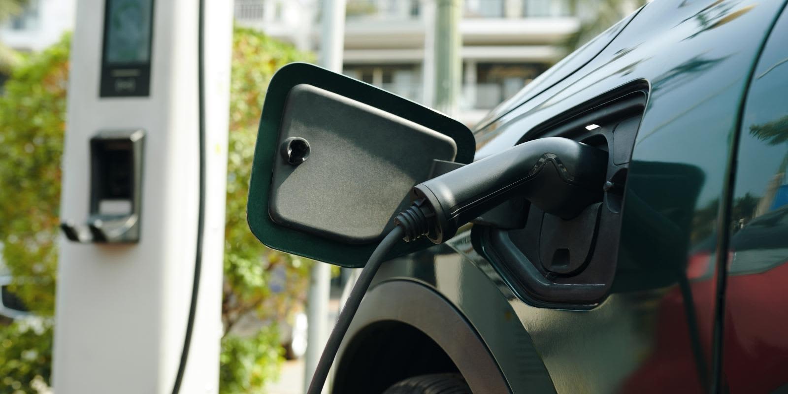 Ein Elektroauto lädt an einer öffentlichen Ladesäule. Im Fokus stehen der eingesteckte Ladestecker und die geöffnete Ladeklappe am Fahrzeug.   