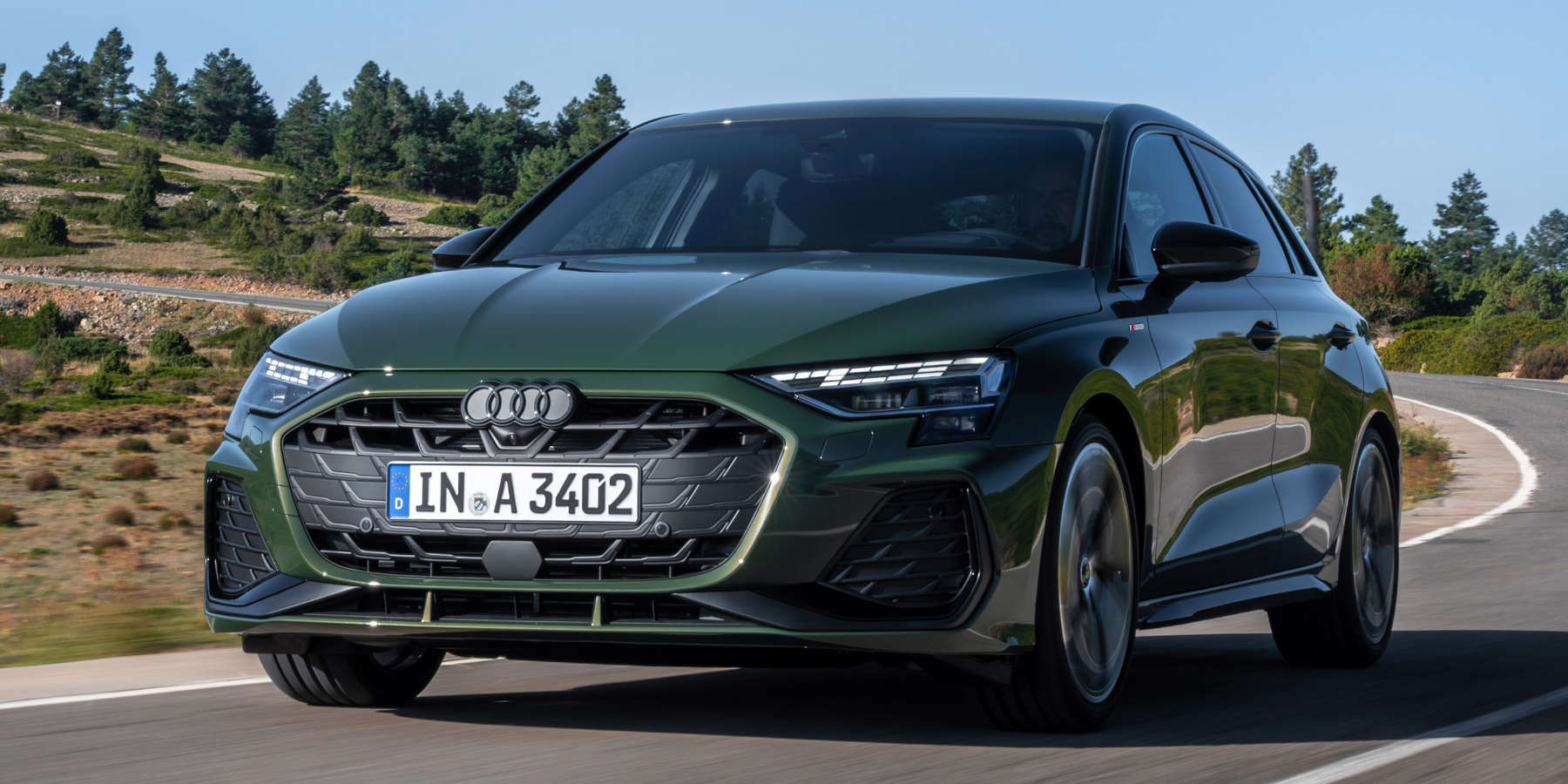 Ein dunkelgrüner Audi A3 Sportback fährt auf einer kurvigen Landstraße. Das Auto hat einen markanten Singleframe-Grill und das deutsche Kennzeichen IN A 3402. (KI-generiert)