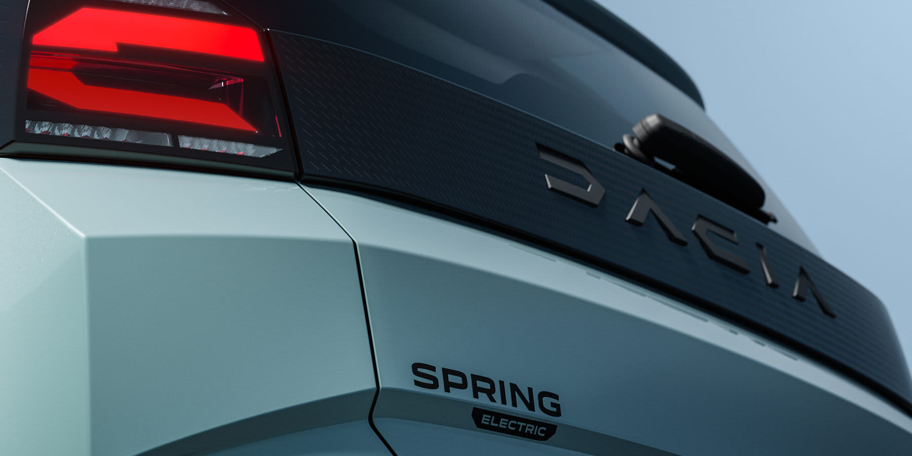 Nahaufnahme des Hecks eines hellblauen Dacia Spring Electric. Zu sehen sind eine rote Rückleuchte, der markante „DACIA“-Schriftzug auf einer schwarzen Blende sowie der darunter liegende Modellname „SPRING ELECTRIC“.
