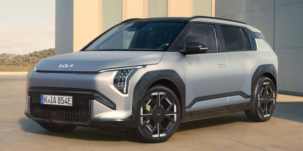 Schrägansicht eines silberfarbenen Kia EV3 GT vor einem modernen Gebäude. Das kompakte Elektro-SUV zeichnet sich durch ein schwarzes Kontrastdach, vertikale LED-Scheinwerfer im „Star Map“-Design und markante Felgen mit neongrünen Bremssätteln aus.