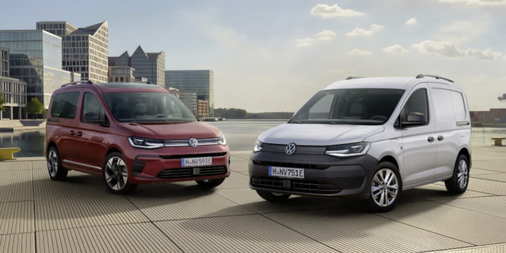 Zwei VW Caddy Modelle (ein roter Pkw und ein weißer Kastenwagen) stehen an einer Hafenpromenade vor einer Stadtkulisse. Beide Fahrzeuge haben ein "E" am Ende des Hannoveraner Kennzeichens.