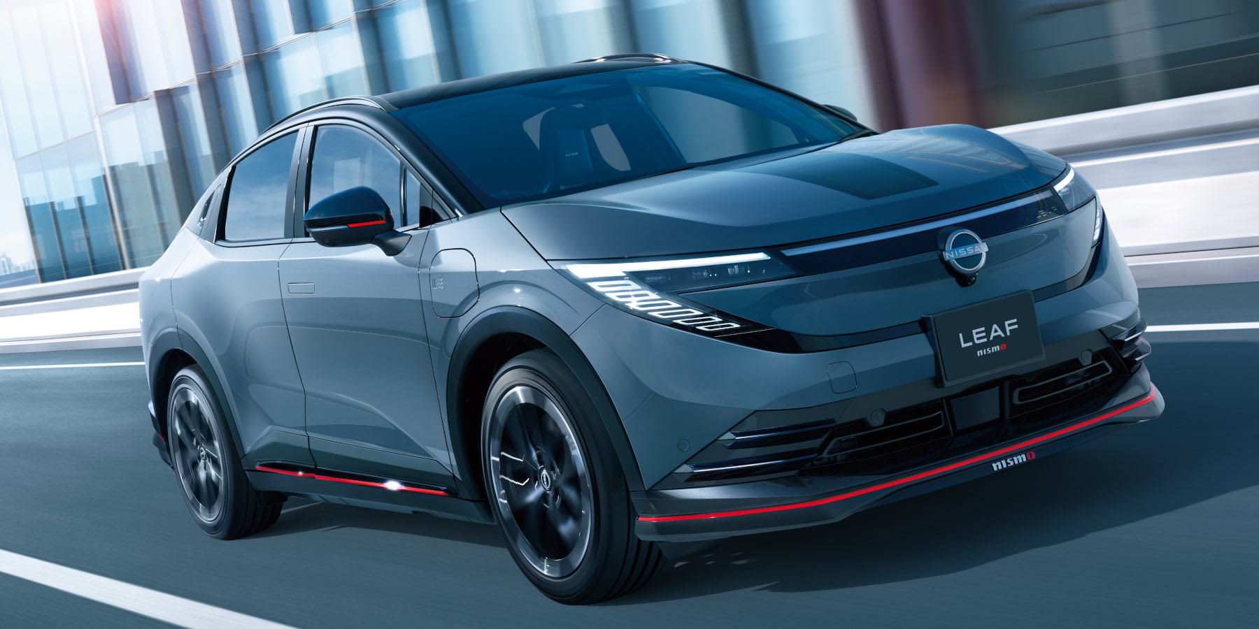 Ein grauer Nissan Leaf Nismo fährt dynamisch an moderner Architektur vorbei. Sportliche rote Akzente an Front und Seitenschwellern prägen das Design. (KI-generiert)