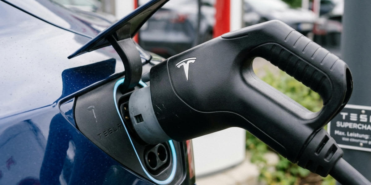 Ein schwarzer Tesla Supercharger-Stecker ist an den Ladeanschluss eines blauen Elektroautos angeschlossen. (KI-generiert)