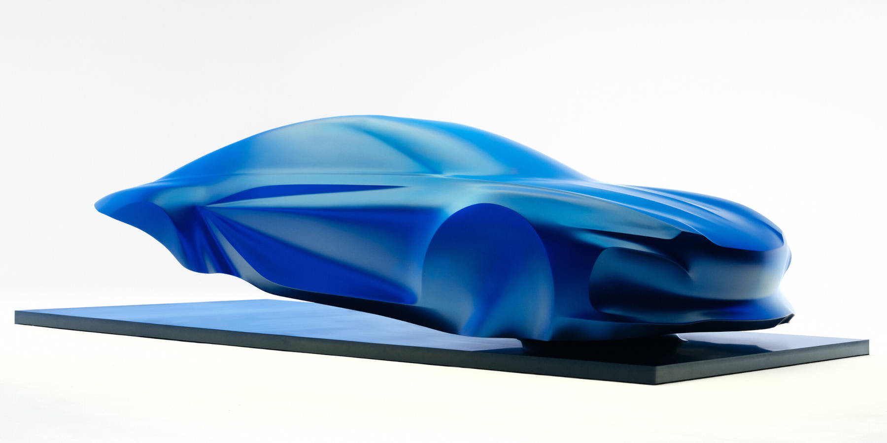 Eine blau schimmernde Designskulptur der Alpine A110 steht auf einem Sockel im Studio. Prägend sind die fließende Form und die aerodynamischen Konturen.   
