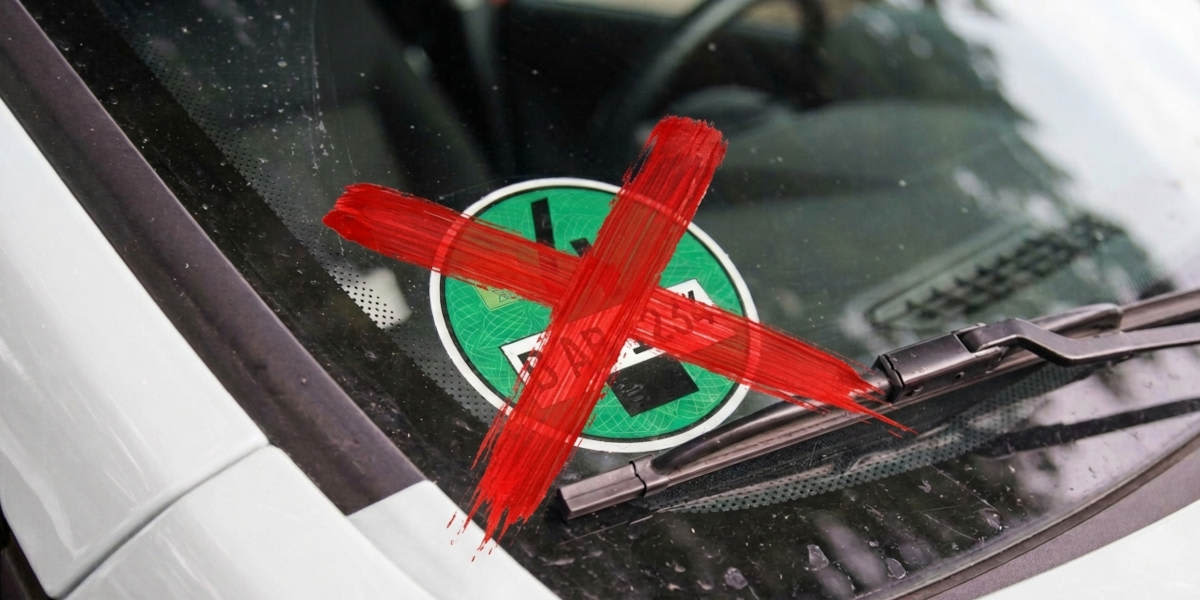 Eine grüne Umweltplakette auf einer Windschutzscheibe ist mit einem roten X durchgestrichen. Das Motiv symbolisiert den Wegfall der Plakettenpflicht.    (KI-generiert)
