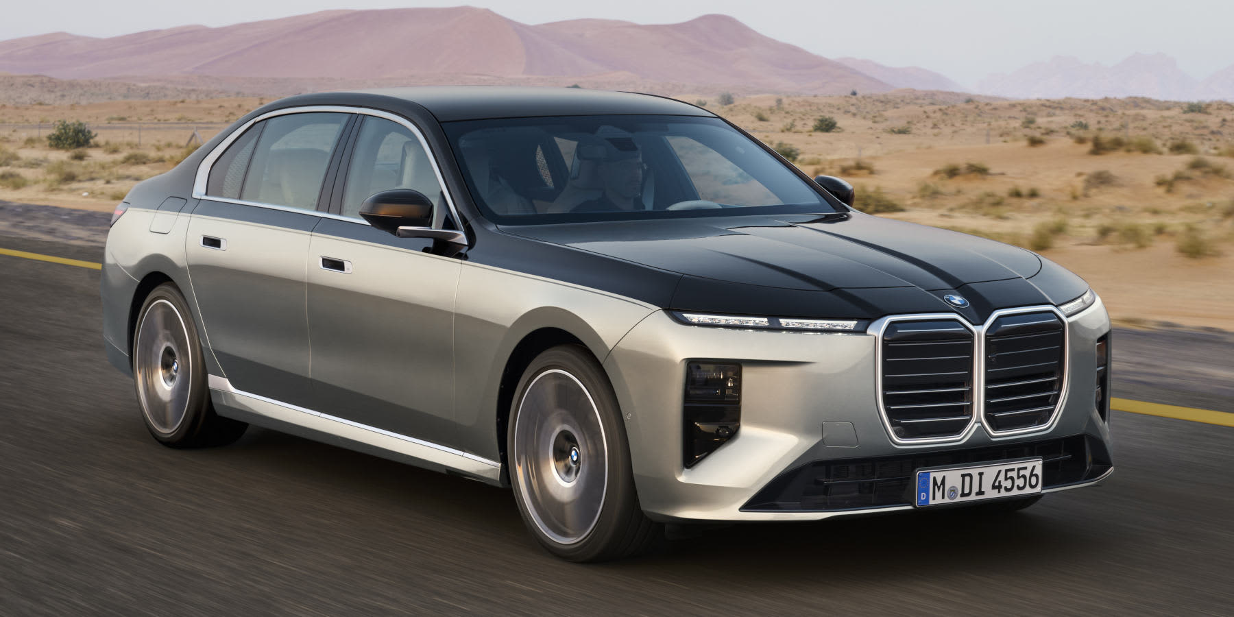 Ein zweifarbiger BMW 740d xDrive fährt durch eine Wüstenlandschaft. Prägend sind die mächtige Niere, zweigeteilte Scheinwerfer und die edle Limousinen-Form.   